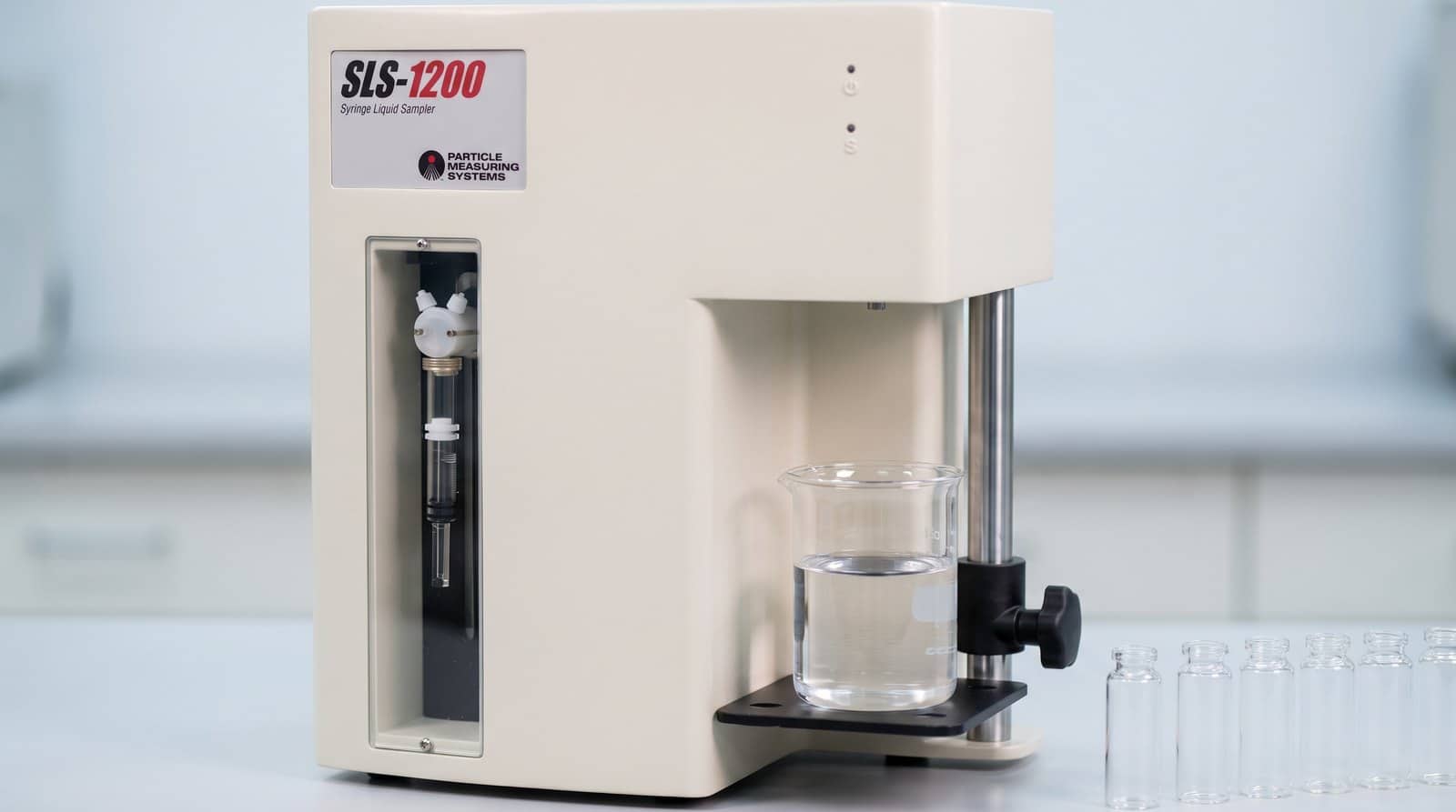 Cận cảnh trạm lấy mẫu của PMS SLS-1200 với cốc thuỷ tinh chứa dung dịch và dãy lọ thuỷ tinh trong suốt bên cạnh