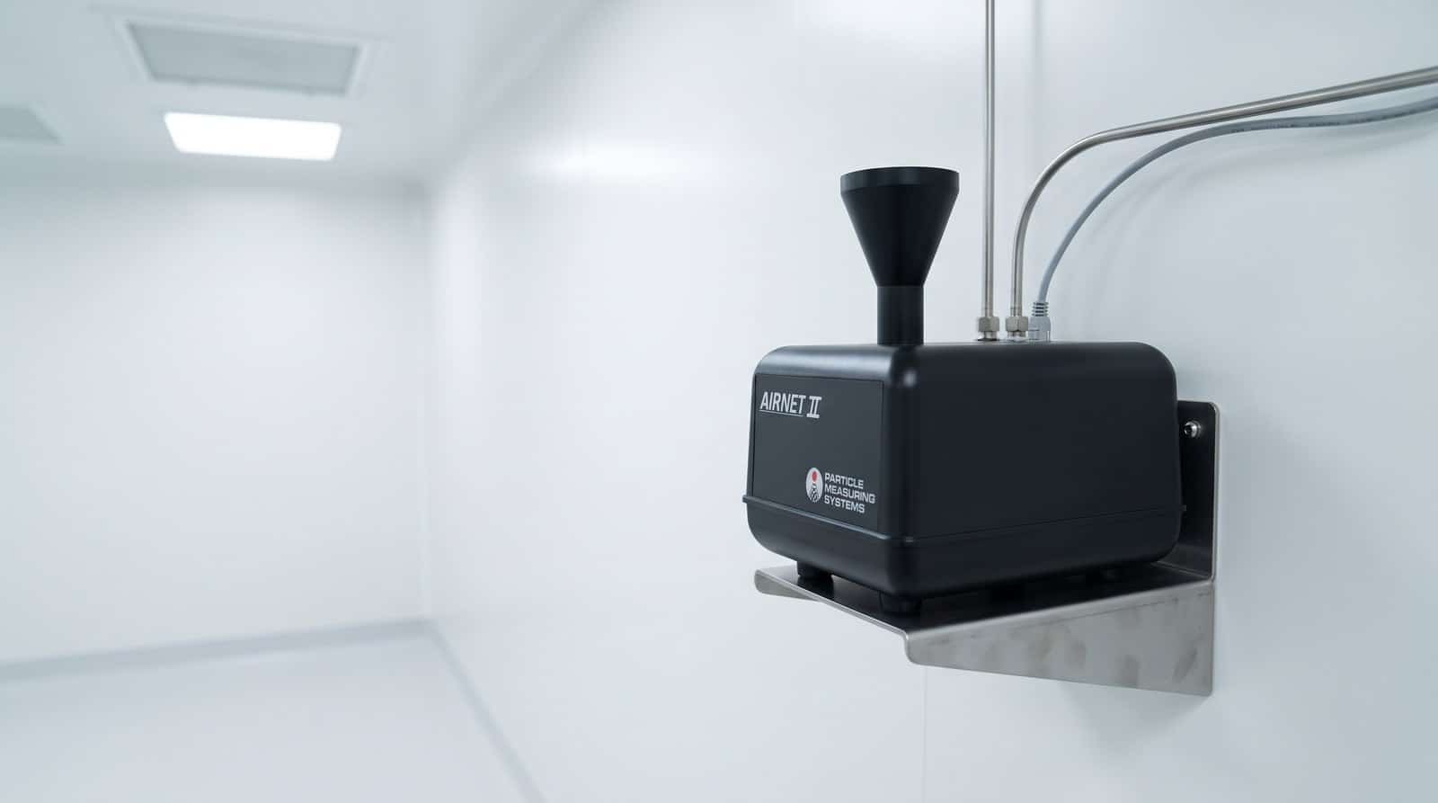 Cảm biến đếm hạt cố định PMS Airnet II 201-4 lắp trên giá đỡ thép không gỉ trên tường phòng sạch dược GMP, phễu lấy mẫu đẳng động học đen trên đỉnh, ống lấy mẫu và cáp mạng đi gọn theo tường