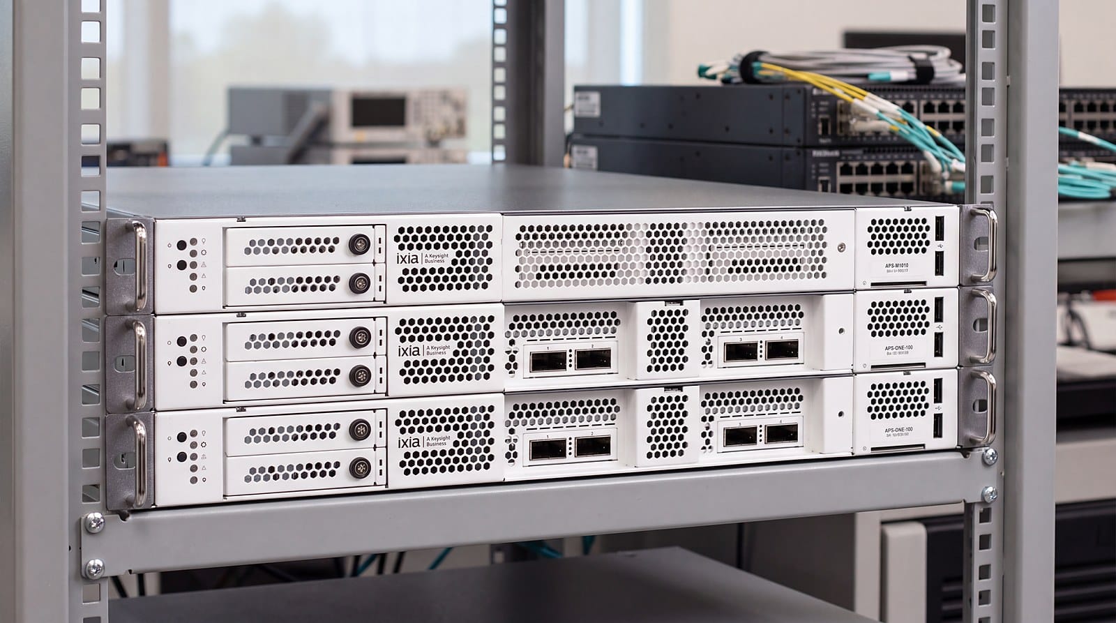 Bộ điều khiển Keysight APS-M1010 và hai node APS-ONE-100 trên kệ rack trong phòng lab kiểm thử mạng