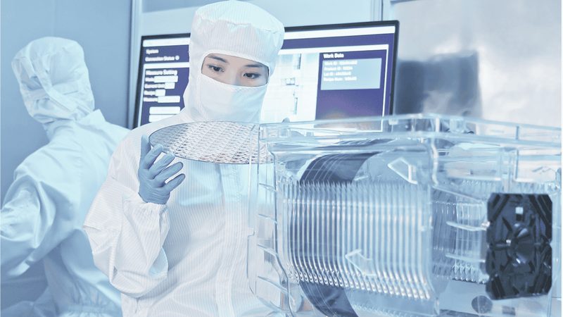 Semiconductor cleanroom technician inspecting a wafer beside a wafer carrier