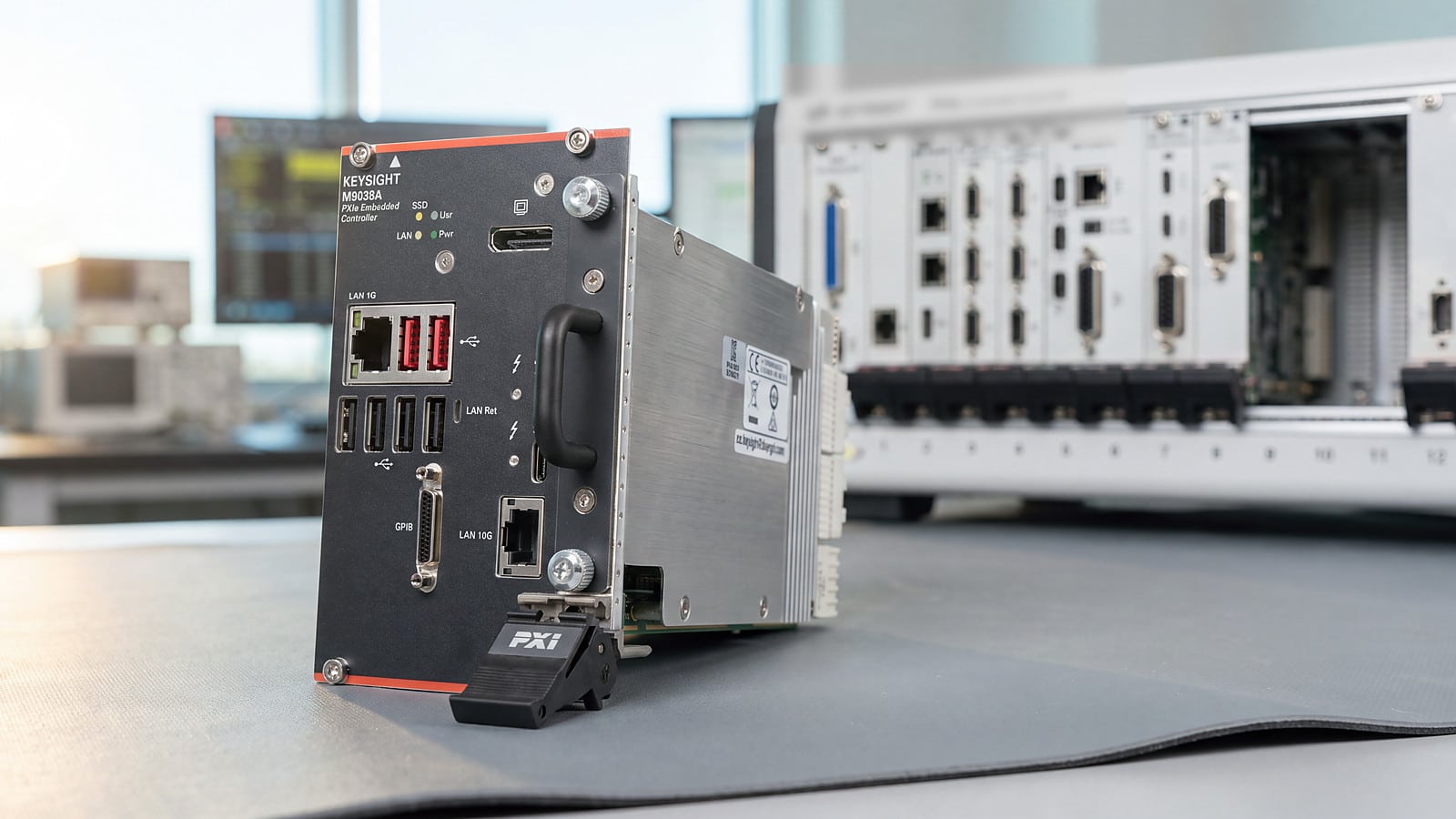 Bộ điều khiển nhúng PXIe Keysight M9038A trên bàn đo phòng lab R&D, phía sau là khung máy PXIe