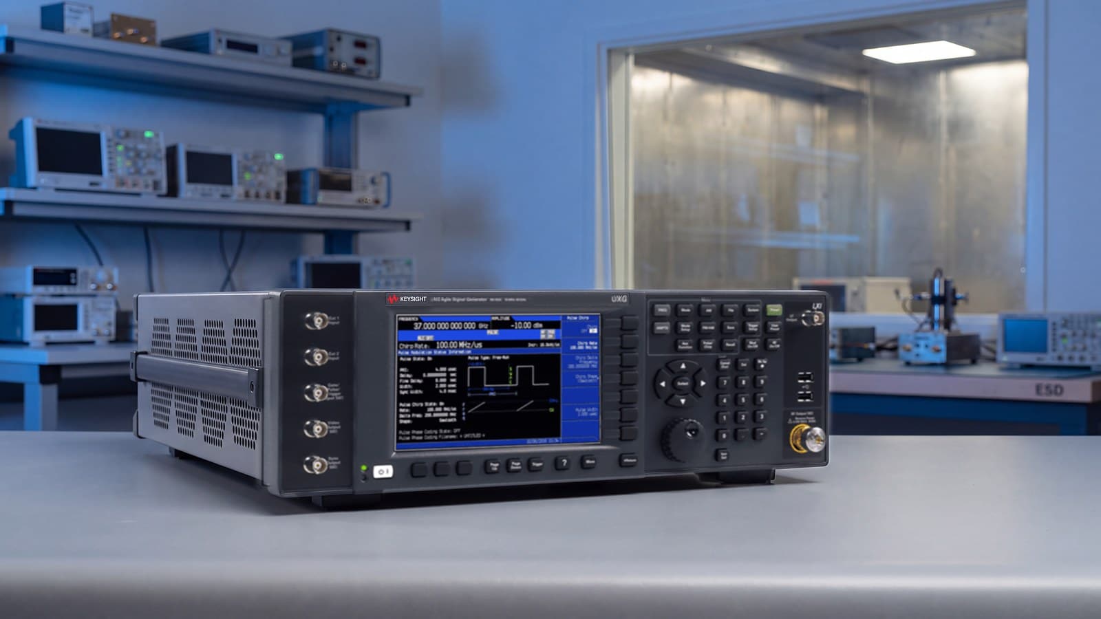 Máy phát tín hiệu agile Keysight UXG N5193A trên bàn đo phòng lab RF vi sóng, phía sau là phòng thử có che chắn